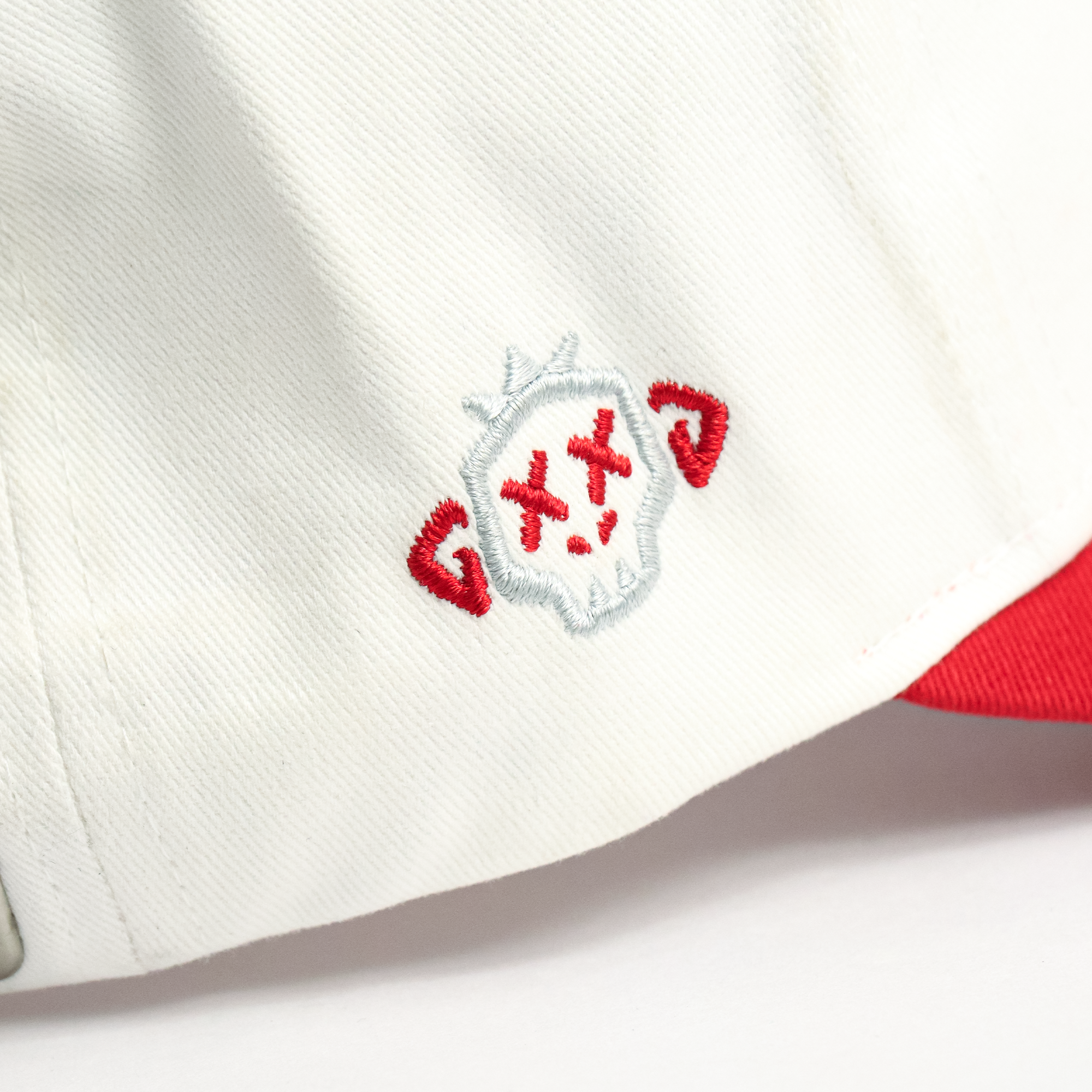 Close-up of a white cap with red and black embroidered logo on a white background